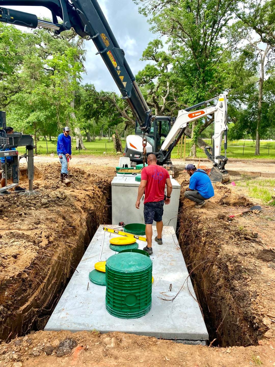 Workers installing green septic tank system in excavated trench with equipment